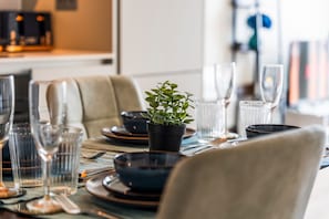 Uma mesa de jantar posta com pratos, copos e talheres, com uma planta em vaso ao centro.