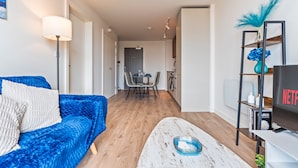 Uma sala de estar moderna com um sofá azul, uma mesa de centro branca e uma TV sobre um suporte.