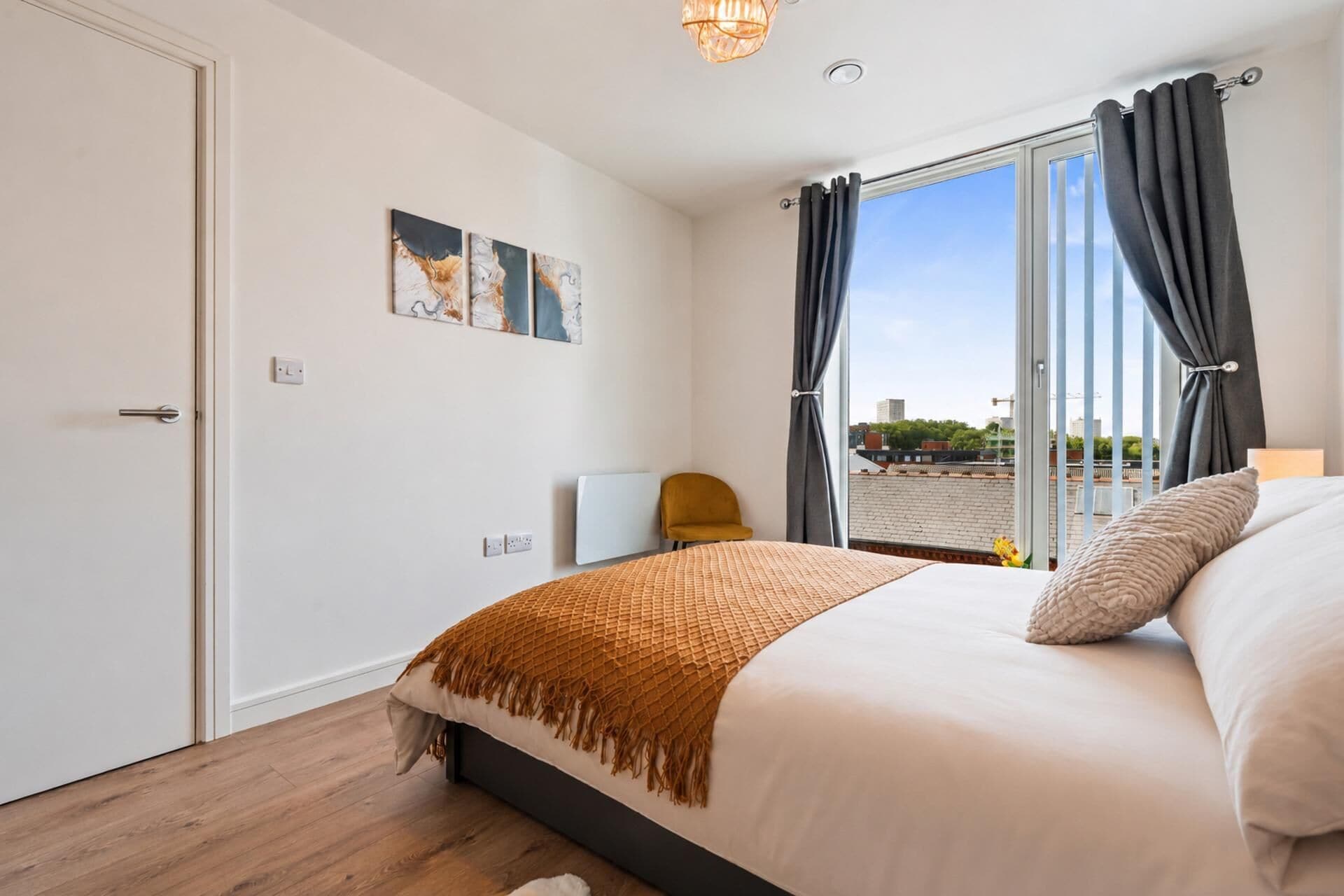 A bedroom with a bed, a chair, a window with curtains, and a city view.