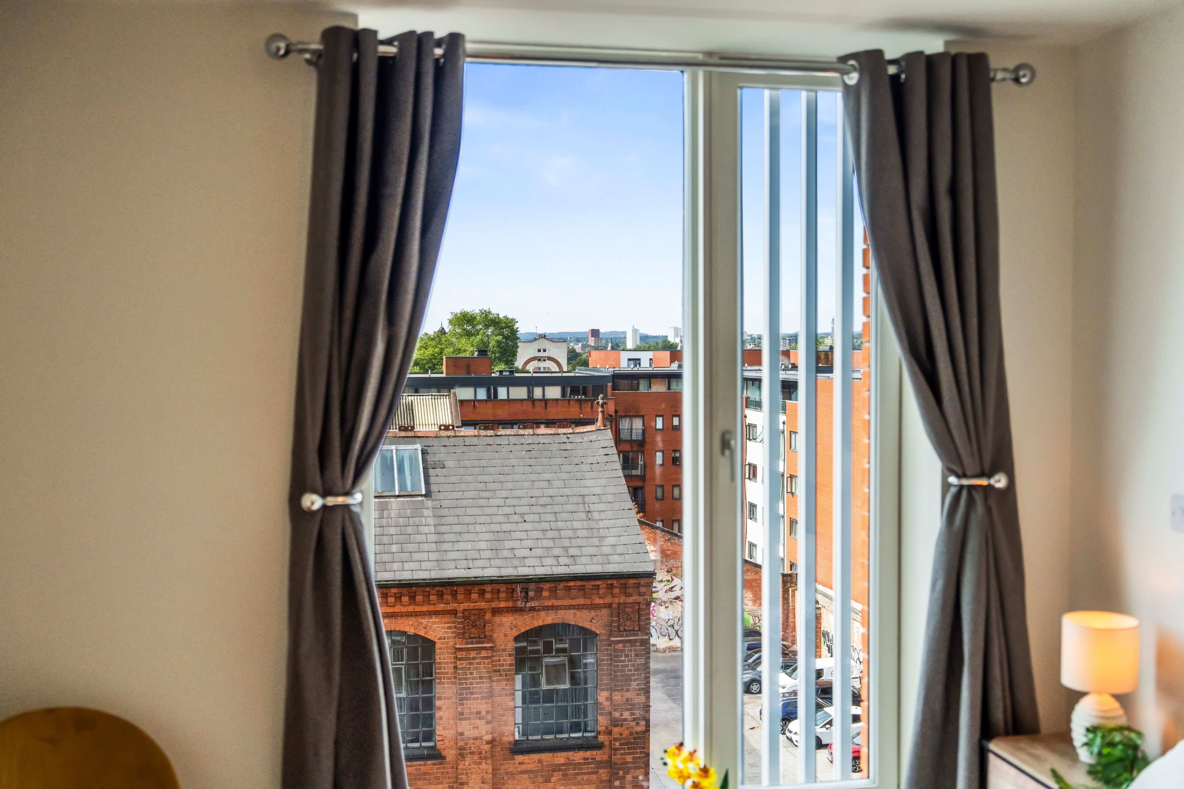 A room with a view of a cityscape through a window with curtains.