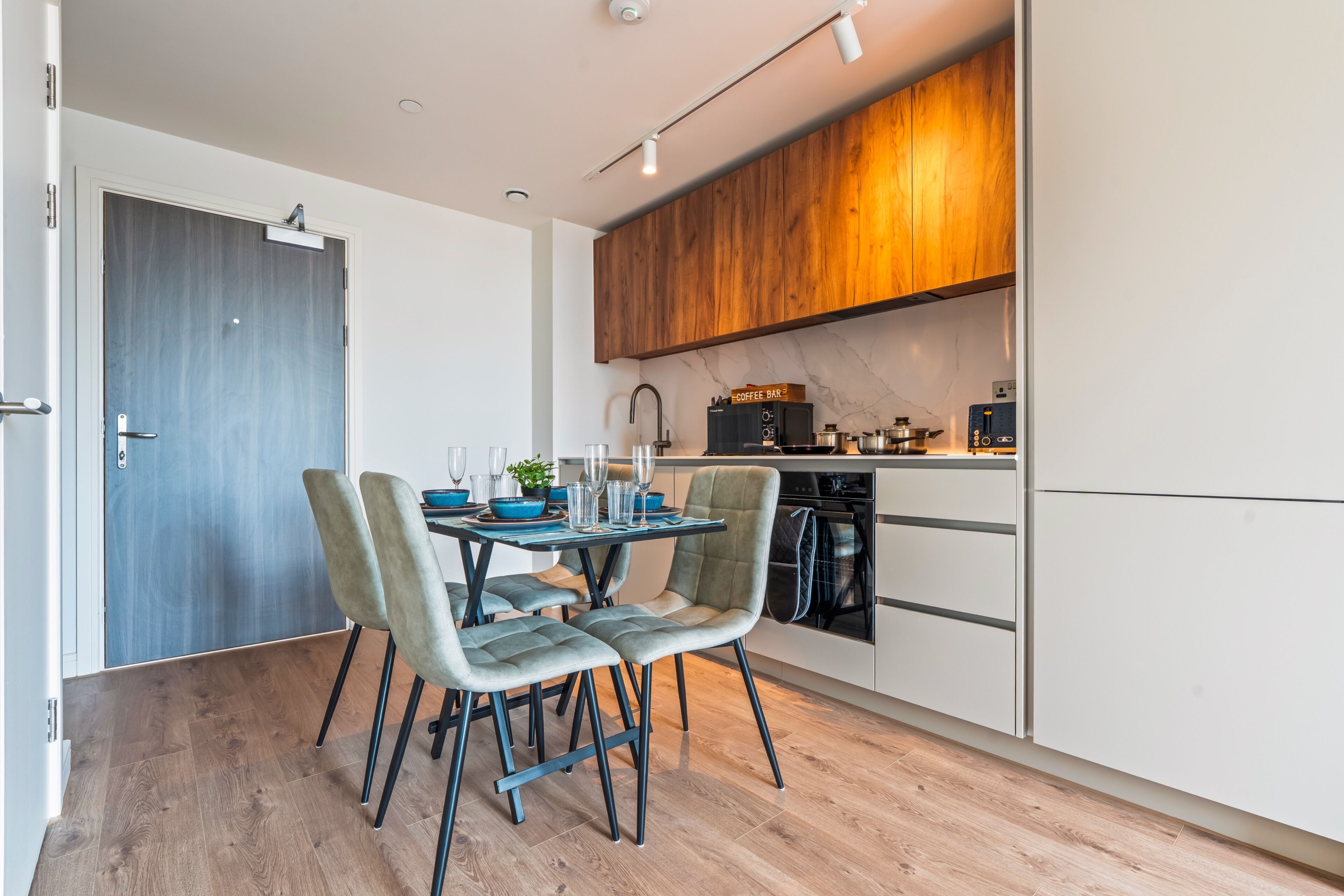 A modern kitchen with a dining area, featuring a wooden cabinet, a coffee machine, and a dishwasher.