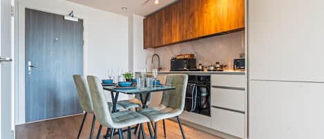 A modern kitchen with a dining area, featuring a wooden cabinet, a coffee machine, and a dishwasher.