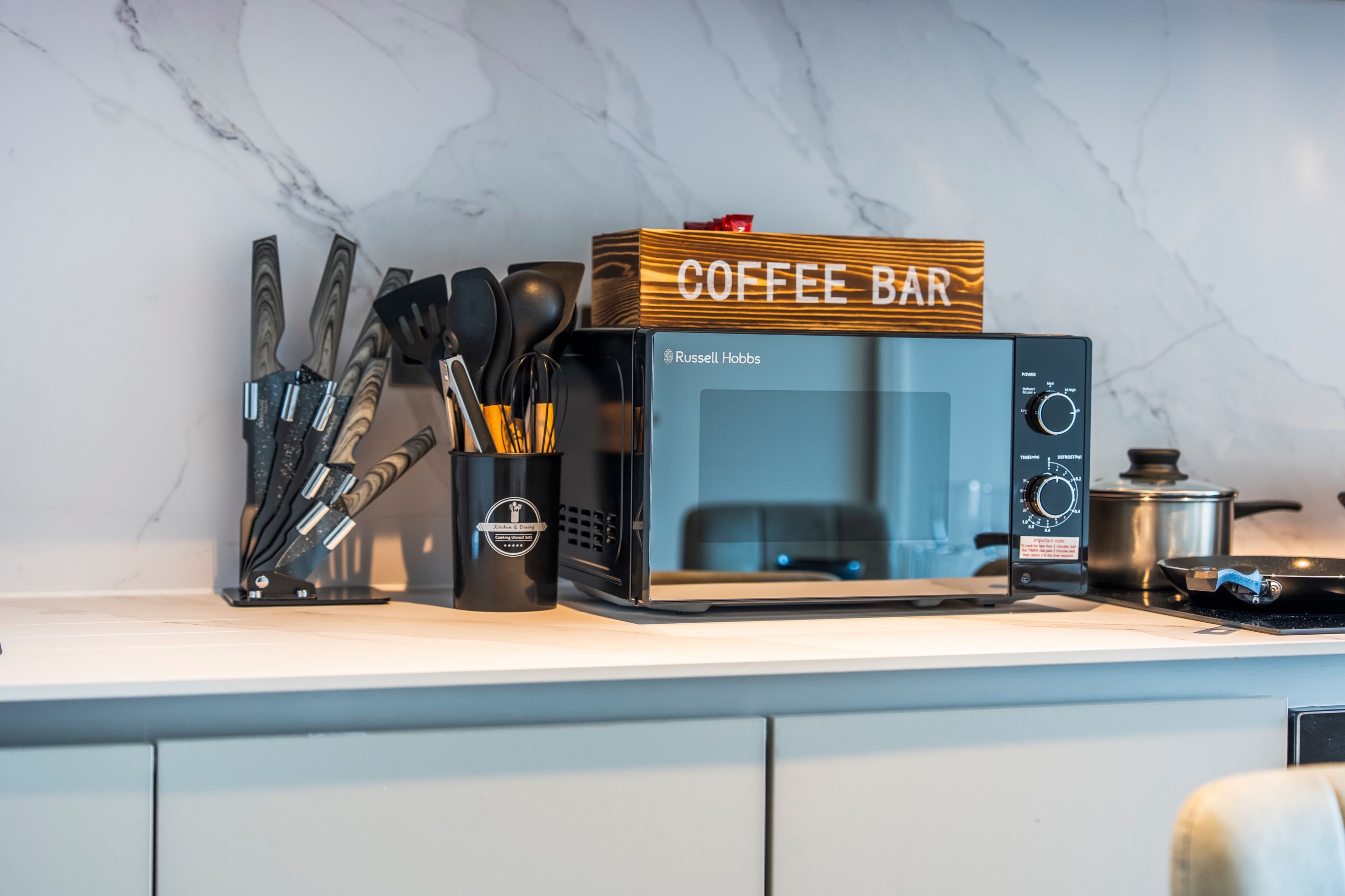 Eine Küchenarbeitsplatte mit einer Kaffeestation, inklusive Mikrowelle, Topf und verschiedenen Küchenutensilien.