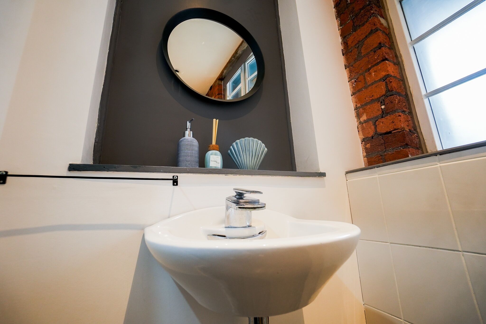 A bathroom with a white sink, a round mirror, and a shelf with toiletries.