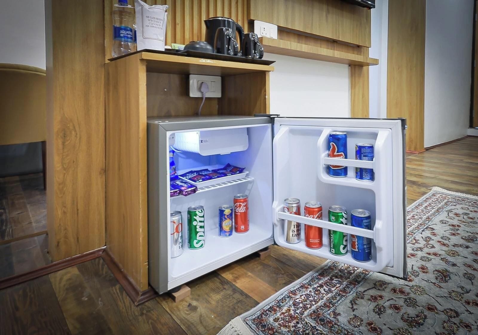 A compact refrigerator with multiple shelves, containing various beverages and snacks.