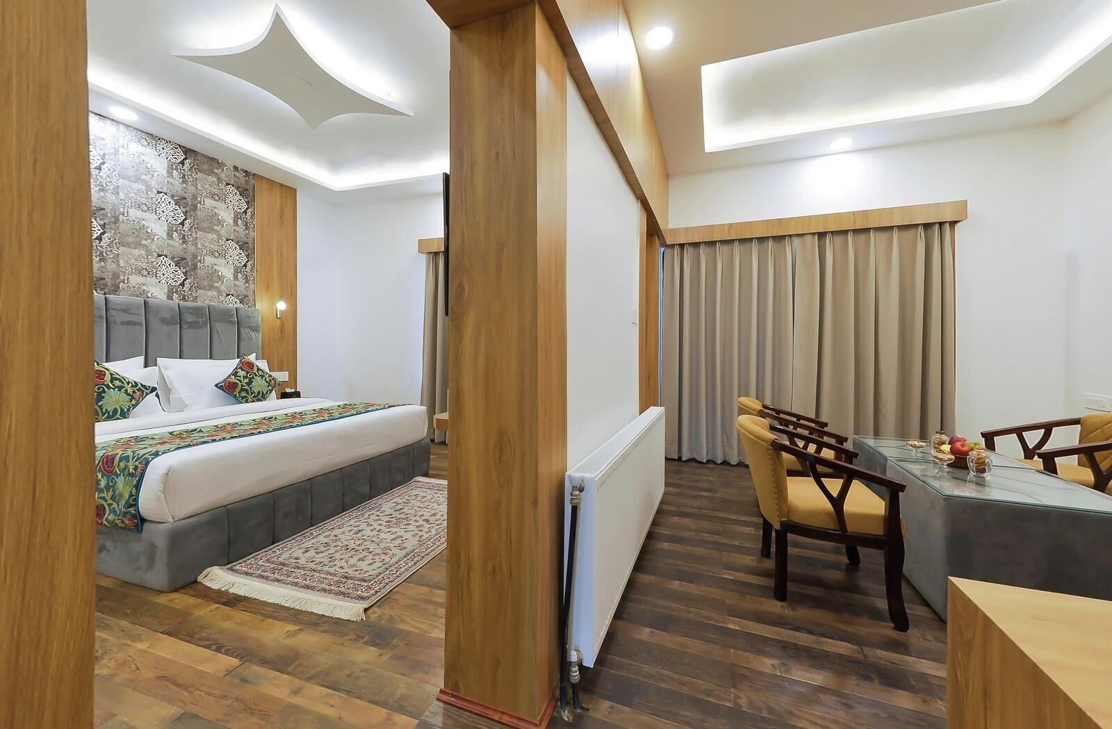 A modern hotel room with a bed, a dining table, and a view of the city.