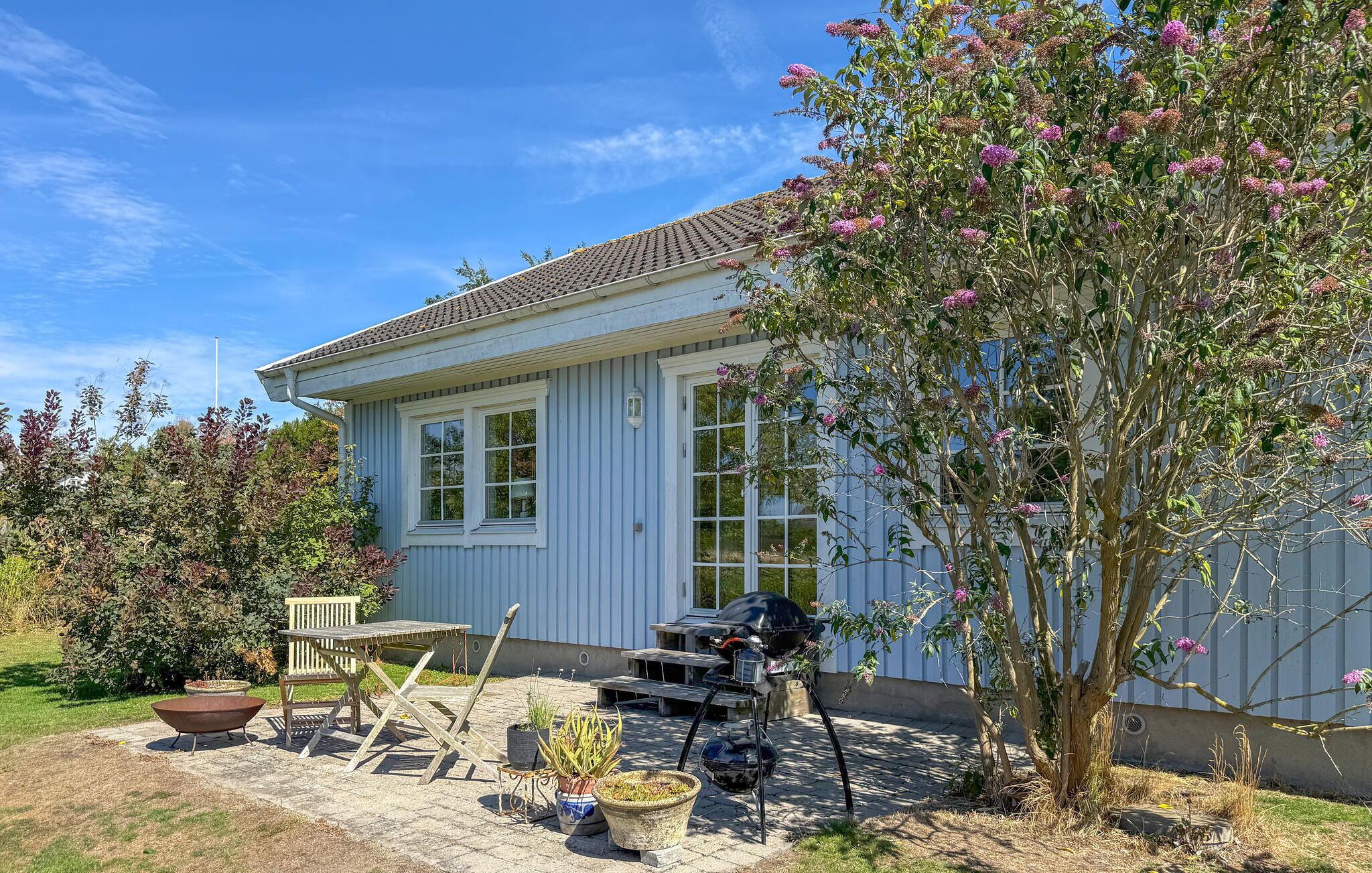 A house with a tiled roof, a front porch with a bench, and a barbecue grill.