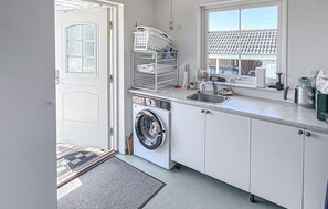 Eine kleine Küche mit Waschmaschine, Spüle und Fenster mit Blick auf eine Wohngegend.