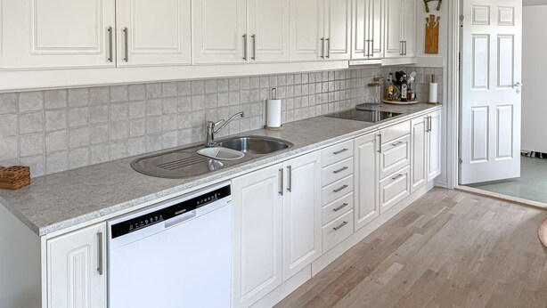 Een keuken met witte kastjes, een granieten aanrecht en een vaatwasser.