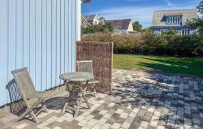Een terras met een tafel en stoelen, een blauwe muur en een tuin met een hek.