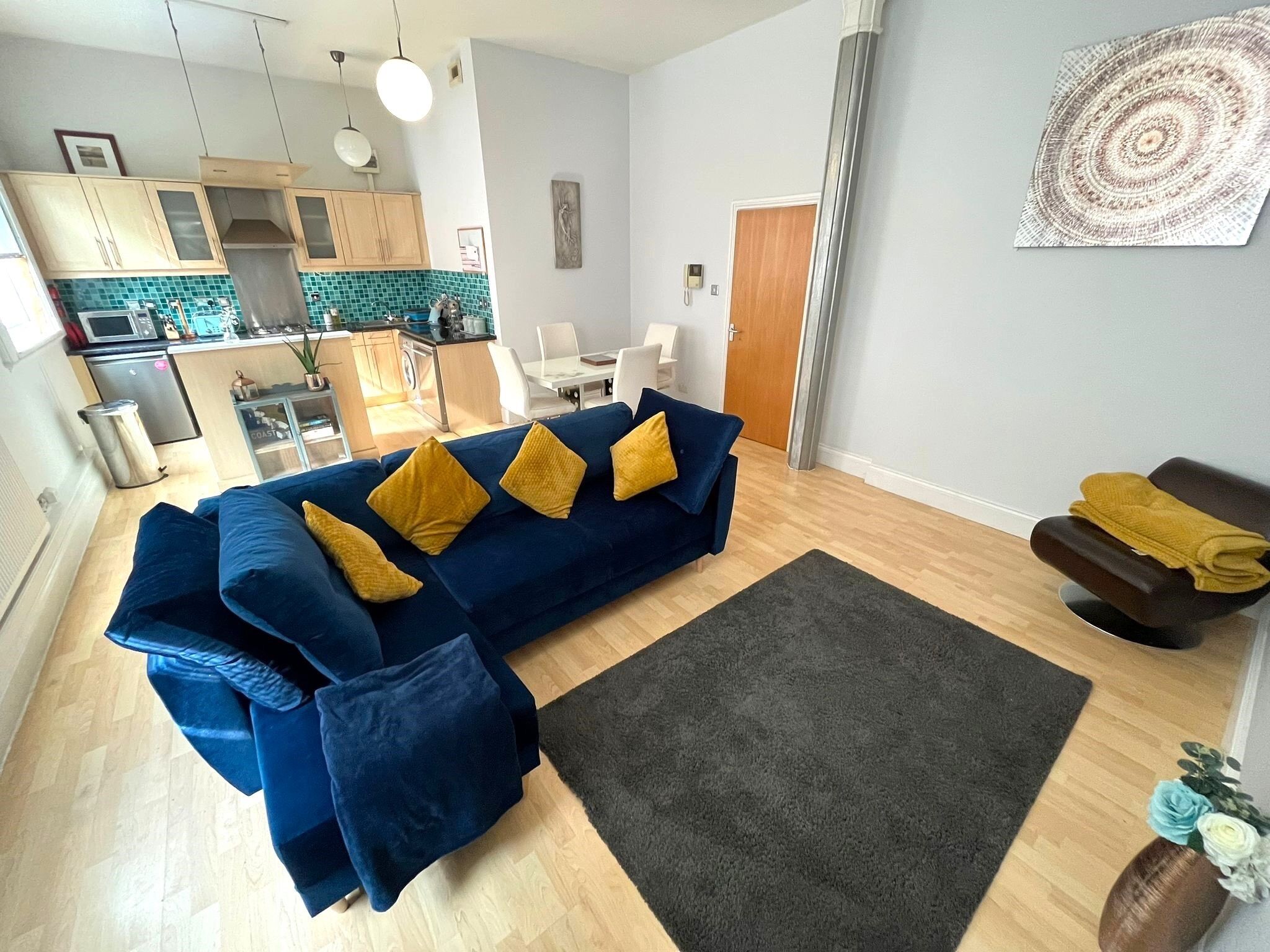 A modern living room with a blue sectional sofa, a dark rug, and a dining area in the background.