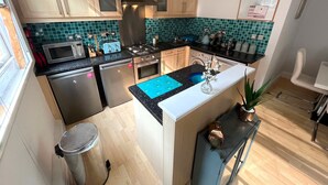 Uma cozinha compacta com uma ilha central, eletrodomésticos de aço inoxidável e azulejos de parede verde-água.