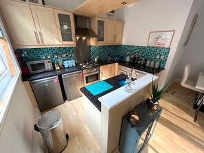 A compact kitchen with a central island, stainless steel appliances, and teal backsplash tiles. - Charming 2 Bedroom Nottingham City Apartment (Nottingham)