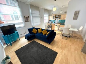 A modern living room with a blue sofa, a black rug, and a teal dresser. - Charming 2 Bedroom Nottingham City Apartment (Nottingham)