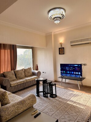 Een woonkamer met een bank, een salontafel, een tv op een standaard, een kroonluchter en een airconditioner.