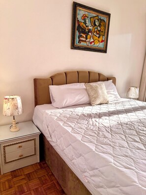 Ein Hotelzimmer mit einem Bett, einem Nachttisch, einer Lampe, einem Bild an der Wand und Holzboden.