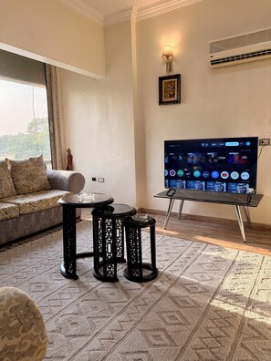 Un salon avec un canapé, une table basse, un téléviseur posé sur un meuble et un tapis à motifs.