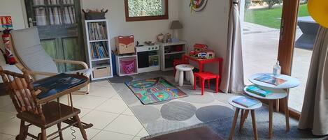 A child's play area with a bookshelf, a toy kitchen set, and a window with a view of greenery.