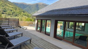A poolside area with lounge chairs, a wooden deck, and a glass-enclosed pool. - 🌟Charming apartment for 4–6 people with parking, a pool, and a terrace with a magnificent view - Arreau🌟 (Arreau)