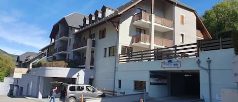 Un edificio de varios pisos con entrada de estacionamiento, un letrero que indica la disponibilidad de espacios y una persona interactuando con un vehículo.