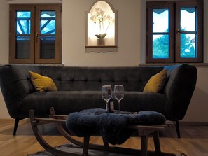 Ein dunkelgraues Sofa mit zwei gelben Kissen, ein kleiner Tisch mit zwei Weingläsern und ein dekoratives Wandbild über dem Sofa.