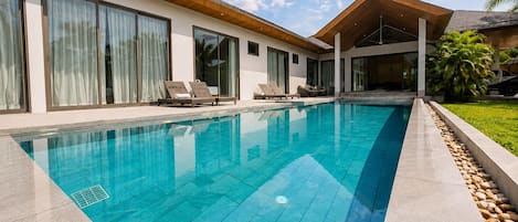 A modern house with a swimming pool, large windows, and a covered outdoor area.