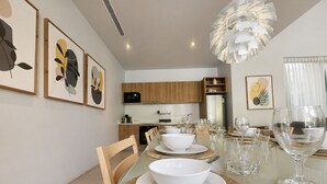 A modern dining area with a glass table, white plates, and clear glassware. - Kamala Grand Estate 5BR Pool Villa (Tambon Kamala)