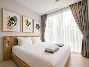 Ein Hotelzimmer mit einem Bett, einem Kopfteil, einem Fenster mit Vorhängen und drei gerahmten Kunstwerken an der Wand.
