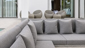 A modern outdoor seating area with a grey sectional sofa and wicker chairs. - Kamala Grand Estate 5BR Pool Villa (Tambon Kamala)