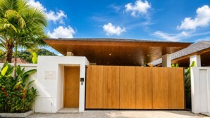 A modern building with a wooden facade, a large overhanging roof, and a gated entrance. - Kamala Grand Estate 5BR Pool Villa (Tambon Kamala)