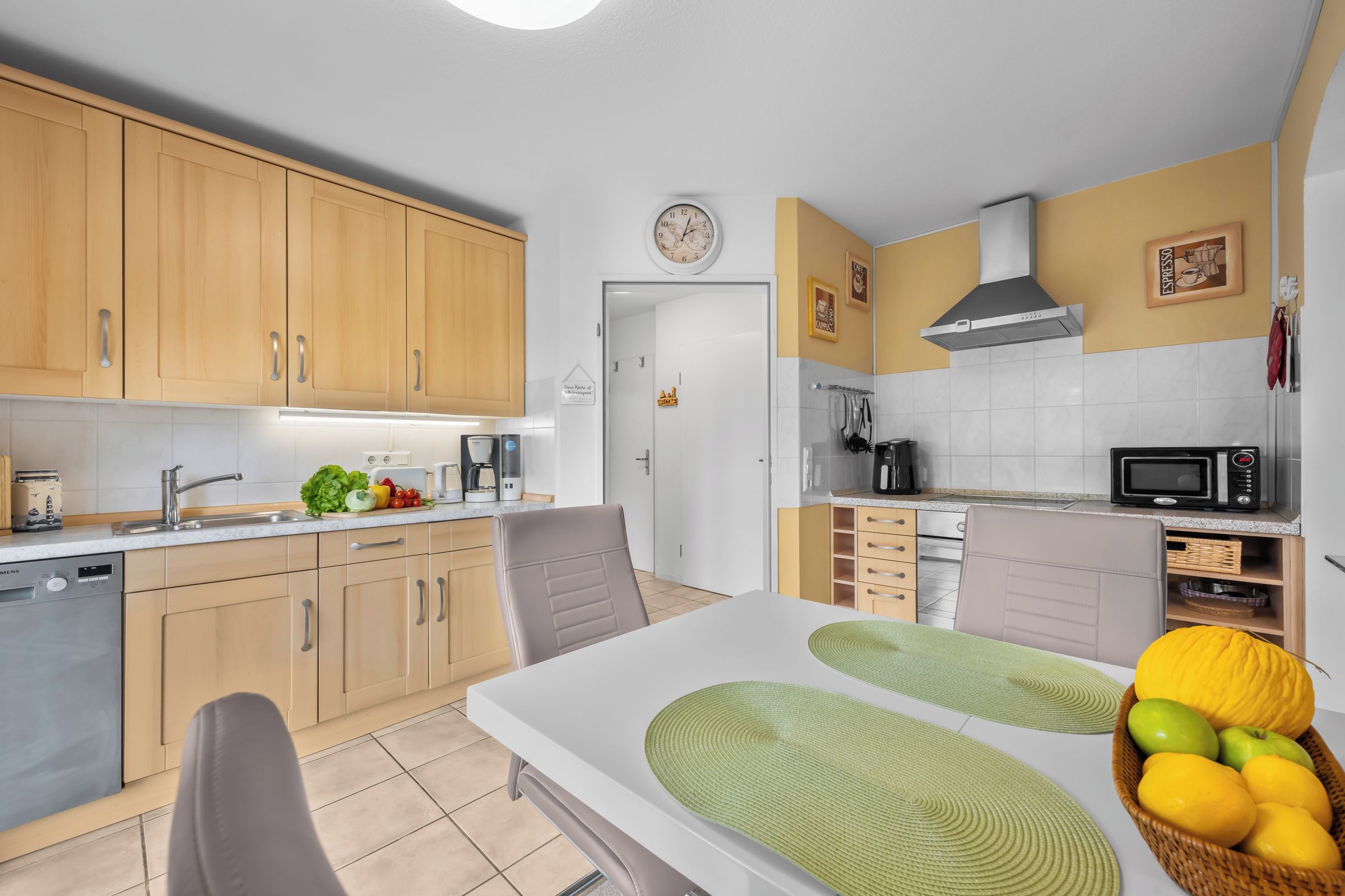 A modern kitchen with wooden cabinets, a microwave, a coffee maker, and a dining area with a table and chairs.