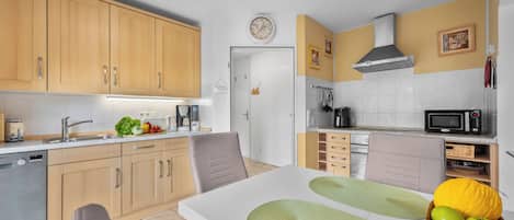 A modern kitchen with wooden cabinets, a microwave, a coffee maker, and a dining area with a table and chairs.