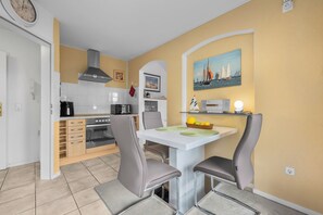 A compact kitchen with a dining area, featuring a microwave, stove, and a painting of sailboats on the wall. - Frische Brise Vacation Rental—Your Vacation Just 100 Meters from the Beach (Schönberg (Holstein))