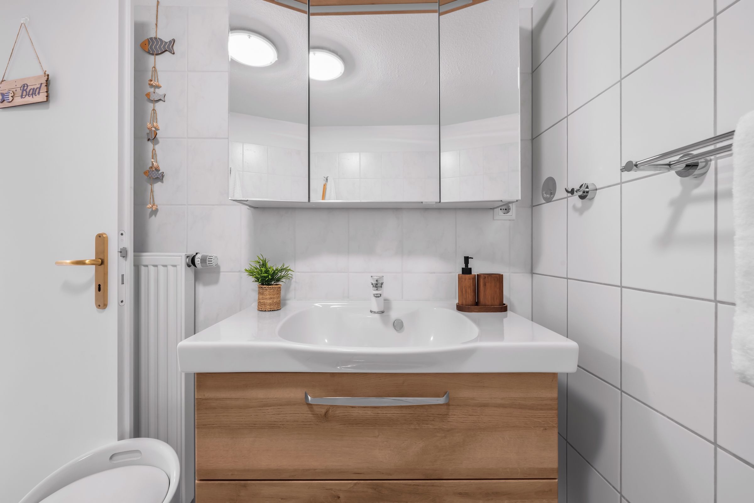 Een moderne badkamer met een witte wastafel, een houten kastje en een spiegel erboven.