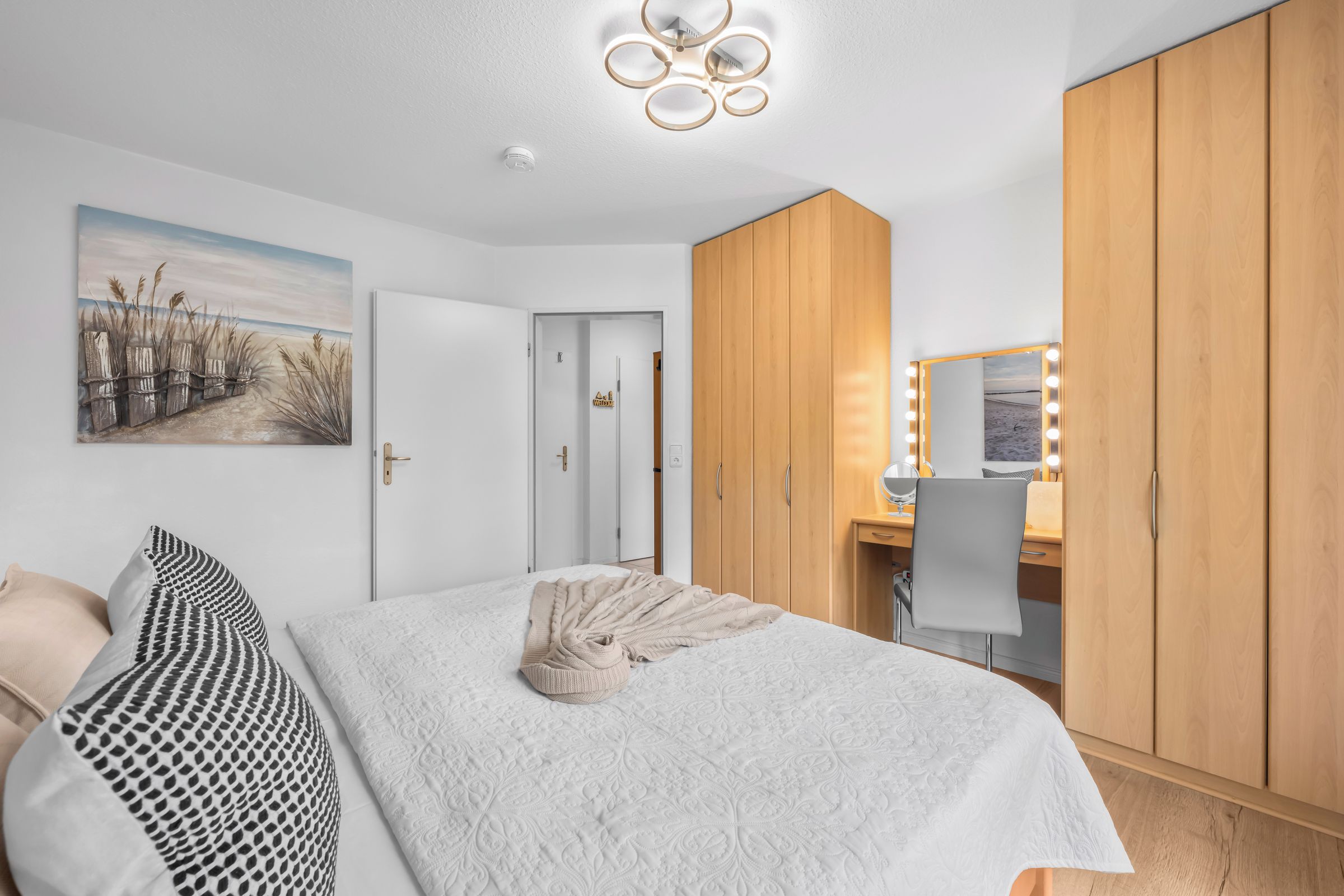 Une chambre à coucher comprenant un lit, une table de chevet, un miroir avec éclairage, une armoire et un tableau accroché au mur.