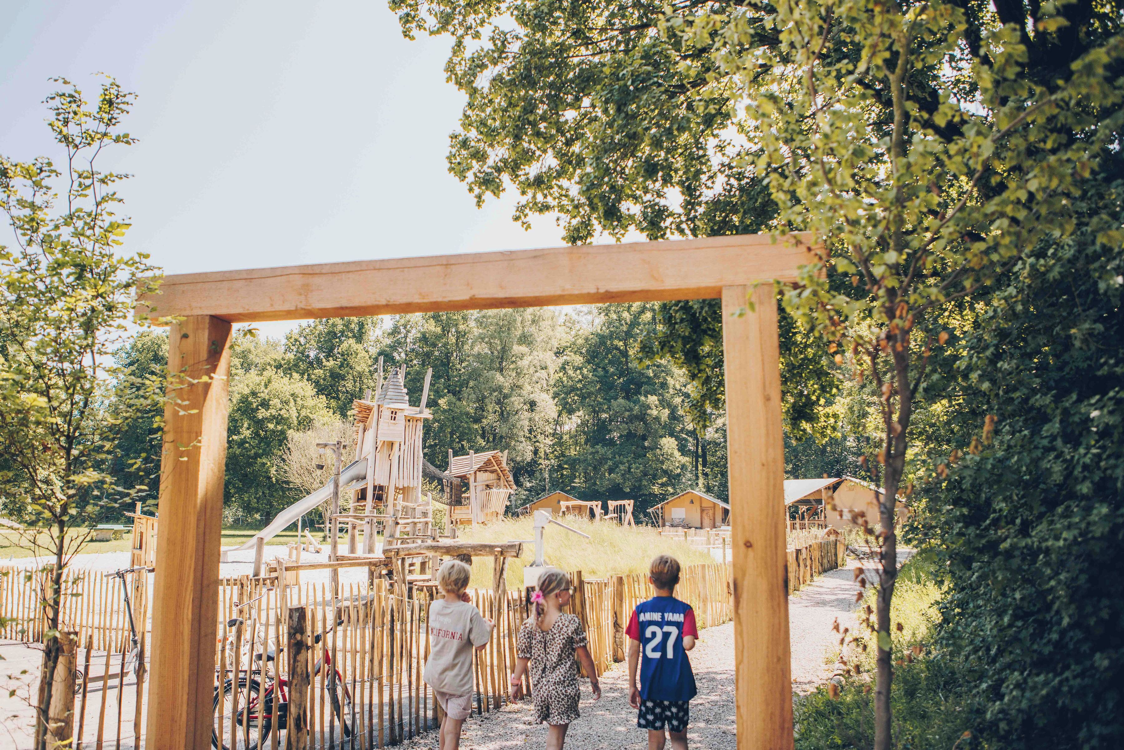 A wooden archway leading to a playground with a slide and climbing structures.