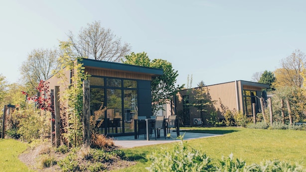 Un bâtiment moderne doté de grandes fenêtres, d’un patio et entouré de verdure.