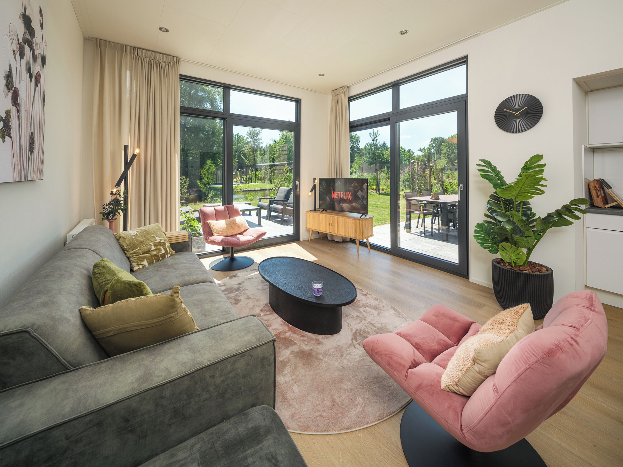 A modern living room with a grey sofa, a pink armchair, and a TV on a wooden stand.
