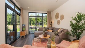 Un salon moderne avec un canapé gris, des fauteuils roses et une table basse ronde. On y trouve également des éléments décoratifs muraux et une plante en pot.
