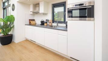 A modern kitchen with white cabinets, a built-in oven, and a large window with blinds.