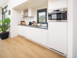 A modern kitchen with white cabinets, a built-in oven, and a large window with blinds.