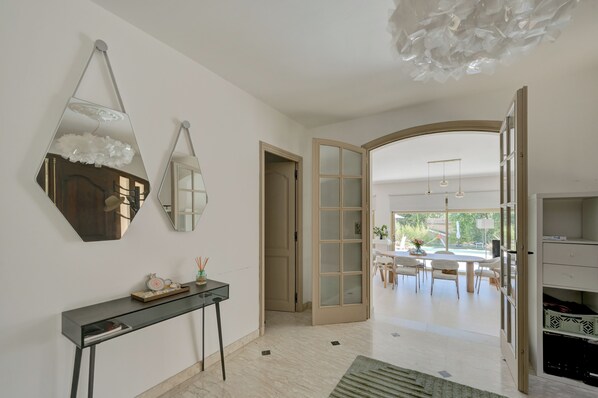 Un intérieur moderne avec une console, deux miroirs fixés au mur, une porte en bois et une vue sur un coin repas.