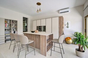 Une cuisine moderne avec un îlot central, des tabourets de bar, une bibliothèque et une plante en pot.
