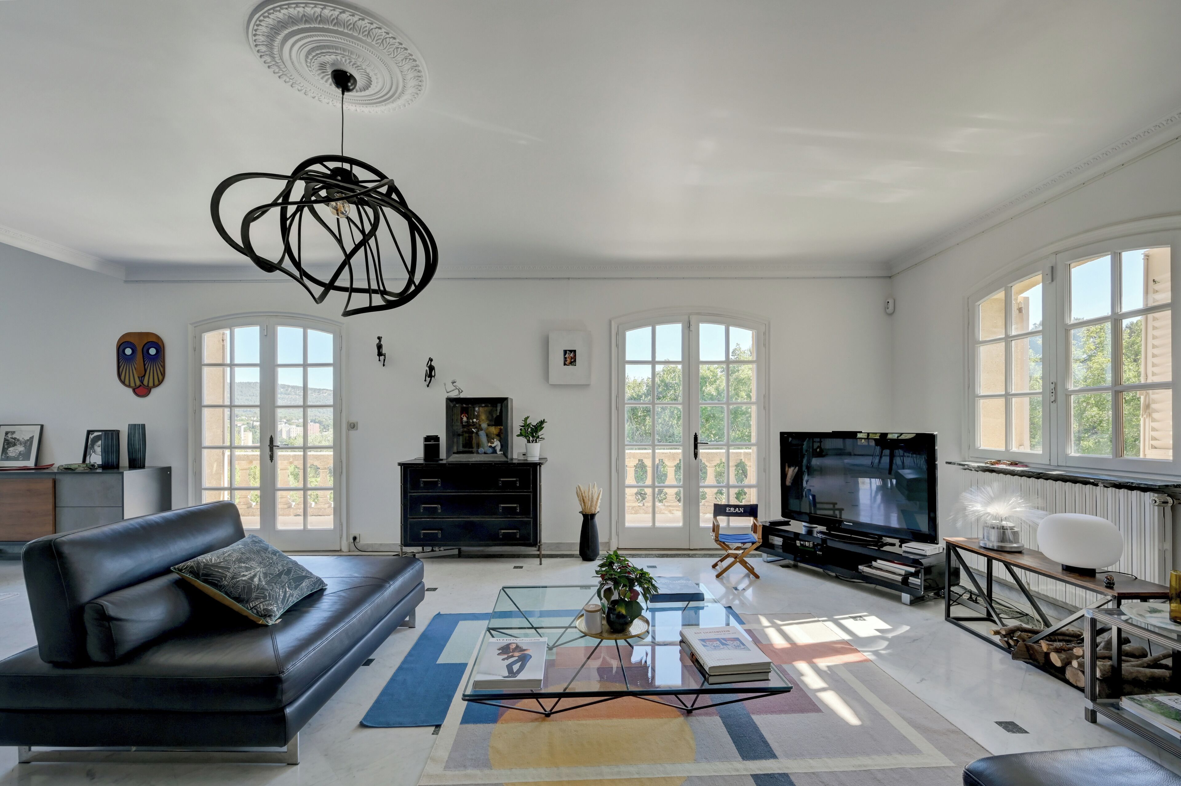 A modern living room with a black leather sofa, a glass coffee table, and a television on a stand.