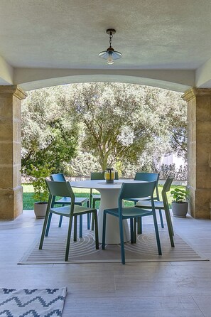 Une terrasse extérieure avec une table et des chaises, un luminaire suspendu et une vue sur les arbres.