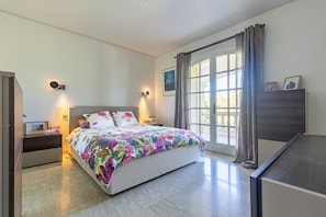 Ein Schlafzimmer mit Bett, Nachttischen, einem Schminktisch, einem Fenster mit Vorhängen und Wandleuchten.
