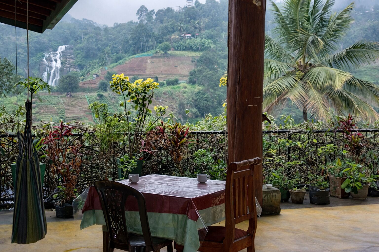 Mesa com toalha, cadeiras e vista para uma cascata e vegetação exuberante.