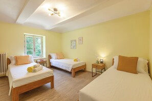 A hotel room with two single beds, a wooden floor, a window with a view of trees, and a ceiling light fixture.
