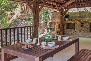 A wooden table set with bowls, a green bottle, and candles in a rustic outdoor setting.