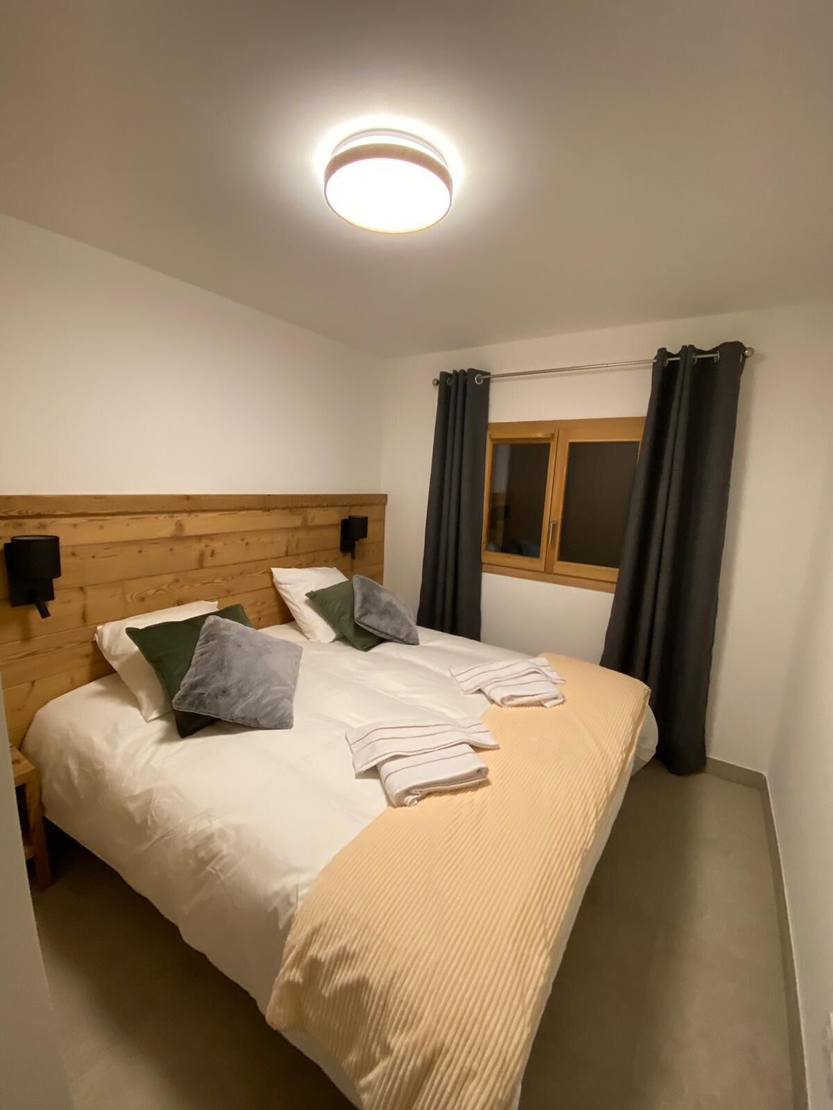 A single bed with a wooden headboard, a bedside table, and a window with curtains.